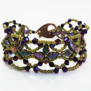 Pode incluir: Uma pulseira de contas com contas de sementes verde-oliva e contas iridescentes roxas e verdes. A pulseira tem um fecho cor de cobre e um design floral. A pulseira tem aproximadamente 18 cm de comprimento.