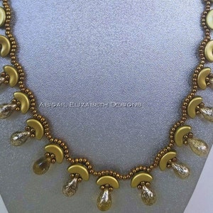 Könnte beinhalten: Eine goldfarbene Halskette mit halbmondförmigen Anhängern und tropfenförmigen Perlen. Die Halskette ist mit kleinen, runden Perlen aufgereiht und hat ein filigranes, aufwendiges Design. Der Text "ABIGAIL ELIZABETH DESIGNS" ist sichtbar.