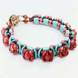May include: A beaded bracelet with red, teal, and gold beads. The bracelet features a floral design with red flower-shaped beads and teal rectangular beads. The clasp is a copper colour.