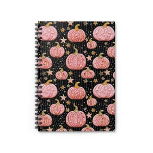 May include: A spiral-bound notebook featuring a black cover with a repeating pattern of light pink pumpkins with gold stems, interspersed with small gold stars and delicate gold dotted lines arranged in a vertical, flowing design across the surface.