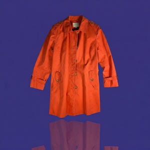 May include: An orange trench coat with a button-up front, shoulder epaulets, and pockets. The coat has long sleeves with buttoned cuffs. The background is a solid blue.