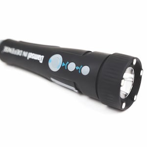 May include: Black flashlight with the text "Damsel in DEFENSE" in white. The flashlight has a textured grip, a bright LED light, and several buttons with blue icons. The flashlight is designed for personal safety.