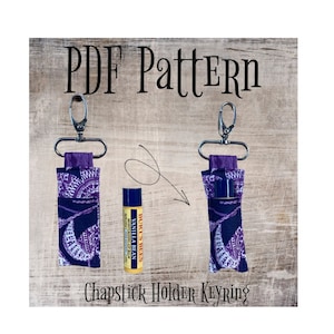 May include: PDF pattern for a purple and white patterned fabric chapstick holder keychain. The keychain has a silver clip and the pattern features a white floral design on a dark purple background. The text "PDF Pattern" and "Chapstick Holder Keychain" are visible in the image.
