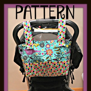 May include: A black stroller with a colorful fabric bag attached to the handle. The bag has a floral pattern with pink, purple, green, and blue flowers on a turquoise background. The bottom of the bag has a geometric pattern with pink, green, blue, and brown squares. The stroller has a black basket underneath.