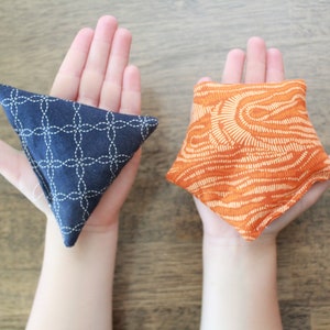 May include: Two fabric bean bags, one blue with a white geometric pattern and one orange with a white abstract pattern.
