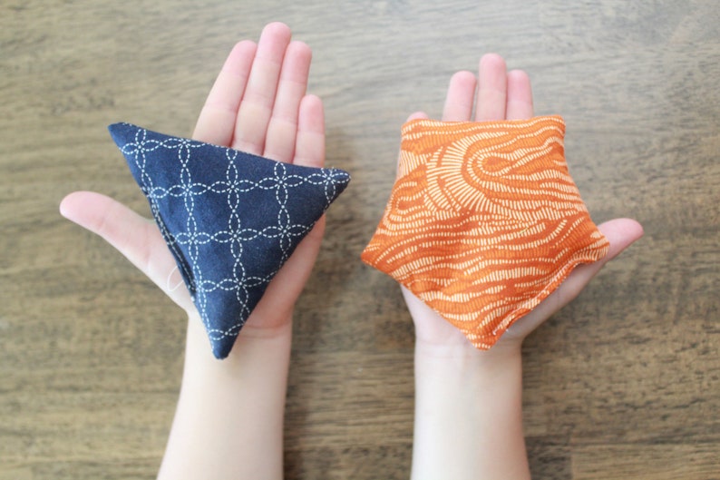 May include: Two fabric bean bags, one blue with a white geometric pattern and one orange with a white abstract pattern.