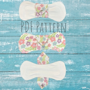 May include: Three white cloth pads with floral print fabric inserts. The pads are folded and laid out on a blue wooden surface. The text "PDF PATTERN" is printed in black on the surface.