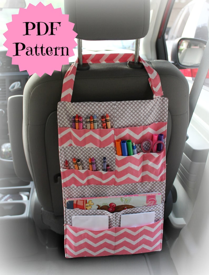May include: Pink and gray fabric car seat organizer with multiple pockets for storing items like crayons, markers, and paper. The organizer hangs from the headrest of a car seat.