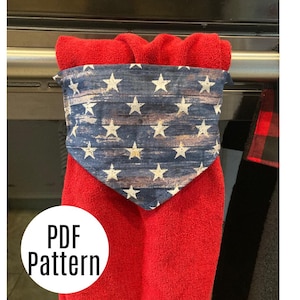 May include: A red kitchen towel with a blue and white bandana-style fabric with stars and stripes hanging on a silver towel rack. The text "PDF Pattern" is on a white circle.