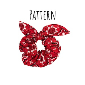 May include: Red bandana print scrunchie with a bow. The scrunchie features a classic paisley pattern in red and white. The word "PATTERN" is written in black above the scrunchie.