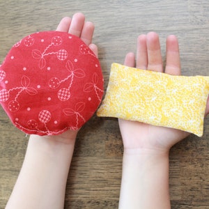 May include: Two fabric-covered hand warmers, one red with a white cherry pattern and one yellow with a white floral pattern.