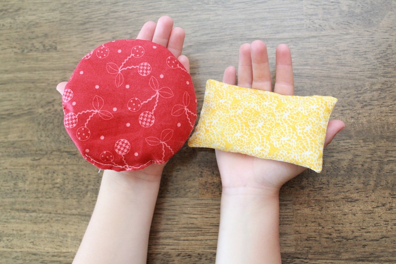 May include: Two fabric-covered hand warmers, one red with a white cherry pattern and one yellow with a white floral pattern.
