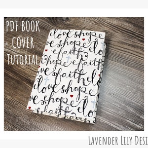 Könnte beinhalten: Ein weißer Stoffbuchumschlag mit einem schwarz-weißen Muster aus den Wörtern "love", "hope" und "faith", die sich wiederholen. Die Wörter sind in einer kursiven Schrift geschrieben und mit kleinen roten Herzen und blauen Kreuzen durchsetzt. Der Text "PDF Book Cover Tutorial" ist oben im Bild in schwarzer Schrift geschrieben.