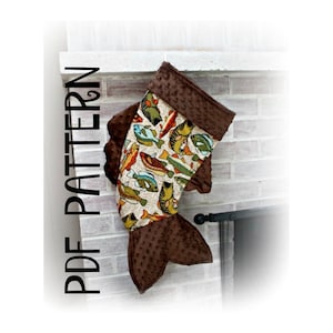 May include: A brown and beige fish-shaped Christmas stocking with a brown fleece lining. The stocking is decorated with a pattern of colourful fish.