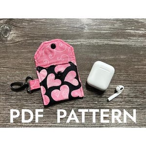 May include: A pink and black fabric case with a heart pattern and a zipper closure. The case is open and a white AirPod case is inside. The text "PDF PATTERN" is at the bottom of the image.