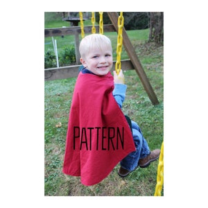 Puede incluir: Un niño con una capa roja con la palabra "PATTERN" impresa, sentado en un columpio al aire libre.