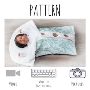May include: A baby swaddled in a white and teal patterned swaddle with wooden buttons. The swaddle has a white faux fur trim. The baby is lying on a wooden surface. The image includes icons for video, written instructions, and pictures.