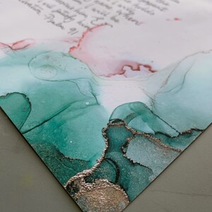 Puede incluir: Primer plano de un papel blanco con un mensaje escrito a mano en tinta negra. El papel tiene un dise&ntilde;o abstracto verde y dorado en la parte inferior.
