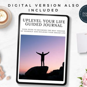 May include: A digital download of a guided journal titled "Uplevel Your Life Guided Journal". The cover features a silhouette of a person with arms outstretched standing on a rock against a pink and purple sunset sky. The text "Your guide to becoming the best version of yourself and building your dream life" is below the title.