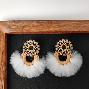 Può includere: Un paio di orecchini di pelliccia bianca con un design circolare intrecciato in marrone e oro.