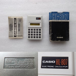 May include: A vintage Casio HL-807 electronic calculator with its original packaging and manual. The calculator is white with black buttons and a digital display showing the numbers 12345678. The packaging is blue and black.