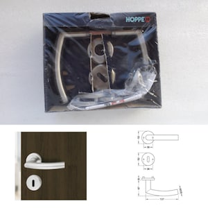 Könnte beinhalten: Ein neues Türgriff-Set in der Verpackung, mit dem Markennamen "HOPPE" sichtbar. Das Set enthält einen Griff, eine Schlüssellochabdeckung und andere Hardware. Der Griff ist silberfarben und hat ein gebogenes Design.