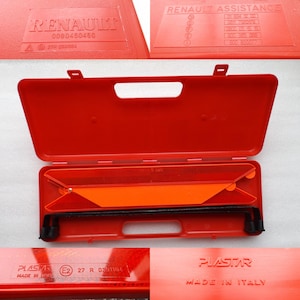 May include: A red plastic case with a reflective orange triangle warning sign inside. The case has a handle and a label that reads "PLASTAR MADE IN ITALY".