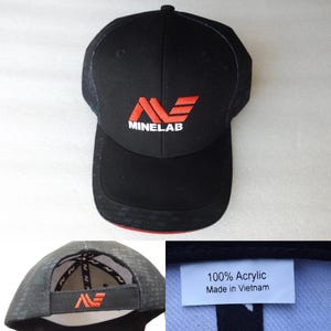 Könnte beinhalten: Schwarze Baseballkappe mit dem rot-weißen "Minelab"-Logo auf der Vorderseite. Die Kappe besteht aus einem strukturierten Stoff und hat einen gebogenen Schirm. Das Etikett lautet "100% Acrylic Made in Vietnam".