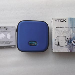 May include: A blue TDK CD wallet with a built-in portable speaker, a user manual, and a box. The box reads "CD wallet with built-in portable Speaker" and has a graphic of a speaker. The CD wallet has a 12 disc capacity.