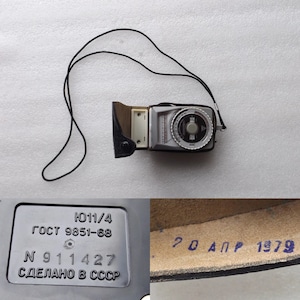 May include: A black and silver light meter with a black leather case and a black strap. The light meter has a dial with numbers and a needle. The case has the text "ГОСТ 9851-68" and "СДЕЛАНО В СССР" printed on it. The case also has the text "20 АПР 1979" printed on it.