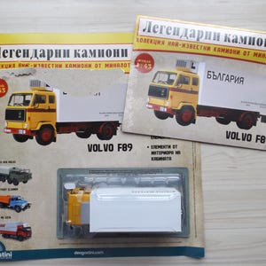 Puede incluir: Un modelo de camión Volvo F89 amarillo y blanco, parte de la colección "Camiones Legendarios". El embalaje incluye el texto "Bulgaria" y "1:43". El modelo está en una caja de plástico transparente.