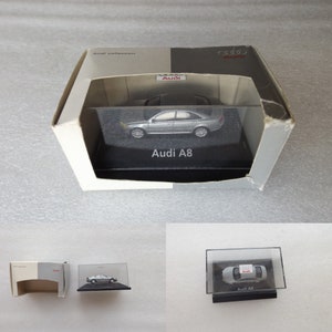 May include: A silver Audi A8 model car in a clear plastic display case. The case sits on a black base with the words "Audi A8" printed on it. The case is inside a white cardboard box with the words "Audi collection" printed on it.