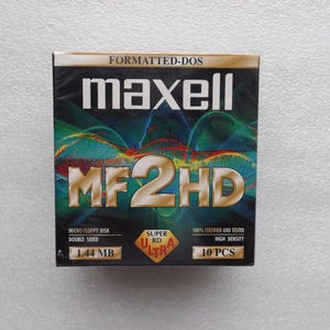 Peut inclure: Une boîte de disquettes micro Maxell MF2HD. La boîte est noire avec le mot "maxell" en blanc et "MF2HD" en or. La boîte porte également les mentions "FORMATTED-DOS", "MICRO FLOPPY DISK DOUBLE SIDED 1.44 MB" et "10 PCS".