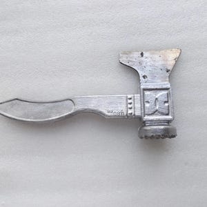Könnte beinhalten: Ein silberner Fleischklopfer aus Metall mit einem gebogenen Griff und einem strukturierten Kopf. Der Kopf hat ein dekoratives Design und der Griff trägt den Text "08H".