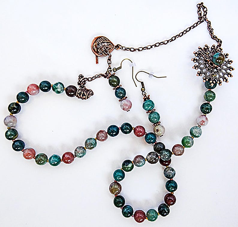 May include: A jewelry set featuring a necklace, bracelet, and earrings. The set includes round beads in shades of green, red, and gray. The necklace and bracelet are connected with gold-colored clasps. The earrings have a hook design.