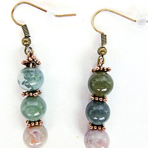 May include: A pair of dangle earrings featuring a combination of green, blue, and pink gemstone beads. The beads are separated by copper-colored decorative elements and suspended from gold-colored ear wires.