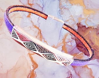 May include: A purple and brown leather bracelet with a silver geometric design. The bracelet is made of two different types of leather, one is a smooth brown leather and the other is a textured purple leather. The silver design is a geometric pattern of diamonds and triangles.