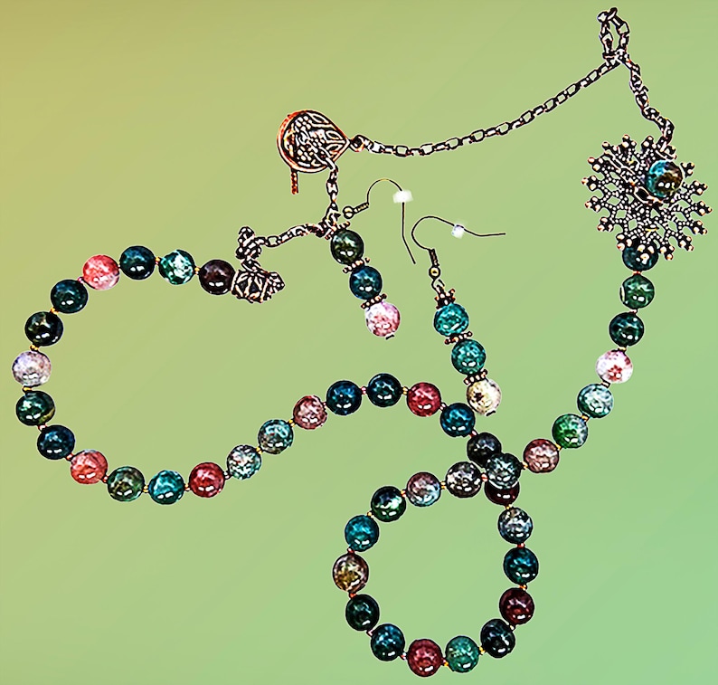 May include: A jewelry set featuring a necklace, bracelet, and earrings. The set includes a necklace with a snowflake pendant, a bracelet, and earrings, all made with colorful, round beads in shades of green, blue, pink, and red. The metal components have a bronze finish.