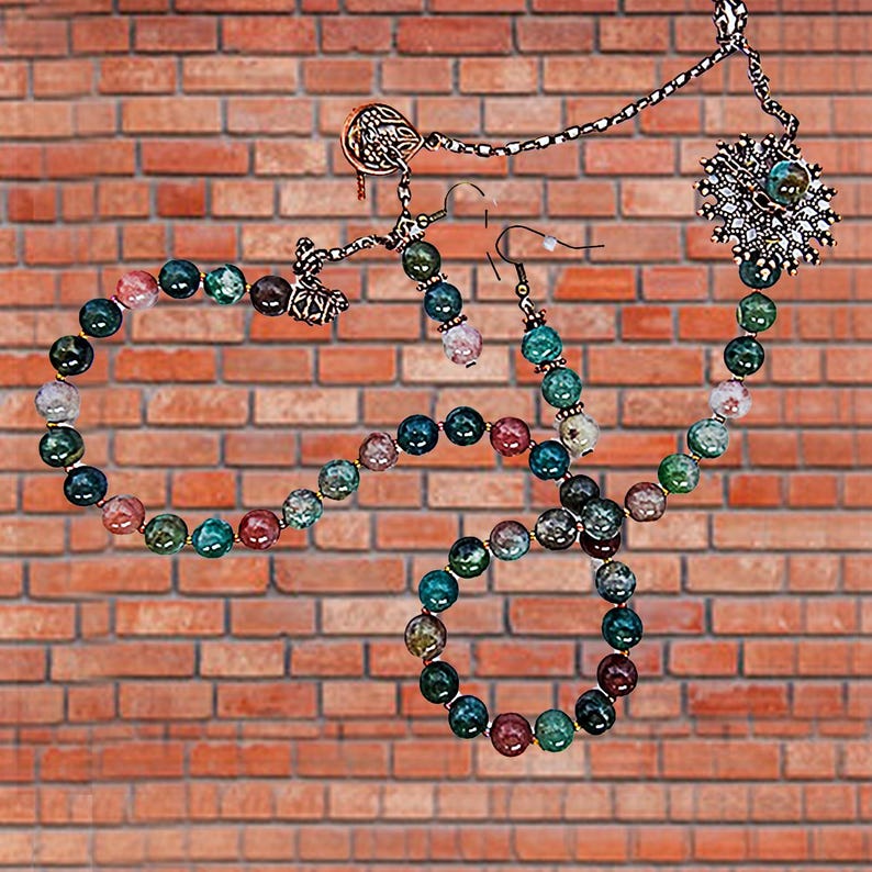 May include: A jewelry set featuring a necklace, bracelet, and earrings with colorful beaded accents. The necklace has a large, ornate pendant. The beads are in shades of green, blue, pink, and brown. The jewelry is displayed against a brick wall.