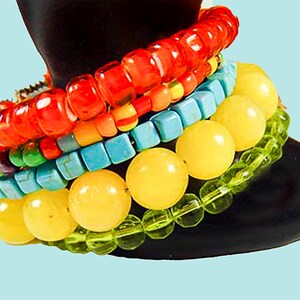 May include: A stack of colorful beaded bracelets, including red, orange, yellow, green, blue, and turquoise beads. The bracelets are layered on a black surface.