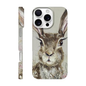 May include: A phone case featuring a watercolor painting of a brown hare with long ears and detailed eyelashes. The case has a light beige background and a side view with floral accents. The design is artistic and nature-themed.