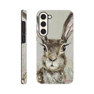 May include: A phone case featuring a detailed painting of a brown hare with long ears and expressive eyes. The artwork has a soft, painterly style with subtle floral accents. The case is shown from multiple angles, highlighting its design and form.