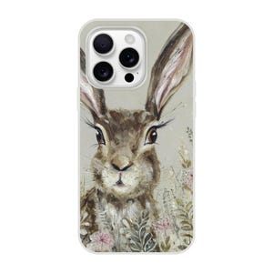 May include: A phone case featuring a watercolor painting of a brown rabbit with long ears and detailed eyelashes. The artwork includes soft green and pink floral accents against a neutral background. The case has a clear border and a camera cutout.