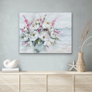May include: A painting depicting a bouquet of white flowers with pink accents in a vase, set against a backdrop of a beach scene with blue water and a sandy shore.