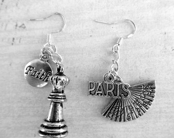 May include: A pair of silver earrings with charms. One earring has a chess piece charm and a round charm with the word "Faith" on it. The other earring has a charm with the word "Paris" on it and a fan-shaped charm.