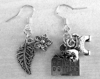 May include: A pair of silver-toned dangle earrings featuring mismatched charms. One earring has a leaf and a flower charm, while the other features a building charm with the word HOSPITAL engraved above the door and a small dog figure attached.