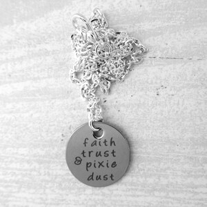 Puede incluir: Collar de plata con un colgante redondo que dice "faith trust & pixie dust".