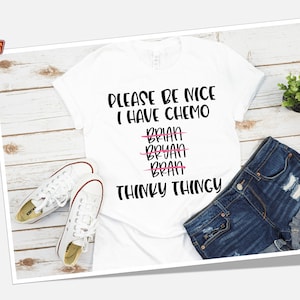 May include: White t-shirt with black text that reads "Please be nice I have chemo" with the word "brain" crossed out multiple times and the words "Thinky Thingy" below.