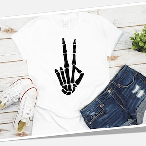 May include: White t-shirt with a black skeleton hand making the peace sign.