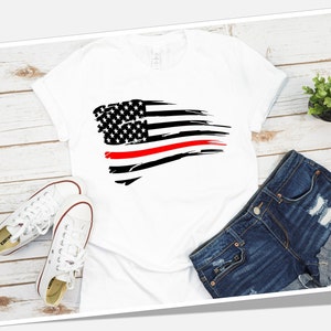 May include: White t-shirt with a black and red distressed American flag design. The flag has a thin red stripe across the middle, representing the "thin red line" of firefighters.